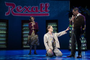  Set at a Rexall store, Aldous Huxley (Harry Hadden-Paton), center, reaches to Gerald Heard (Robert Sella) with Maria Huxley (Laura Shoop) at rear. (Photo by Joan Marcus)